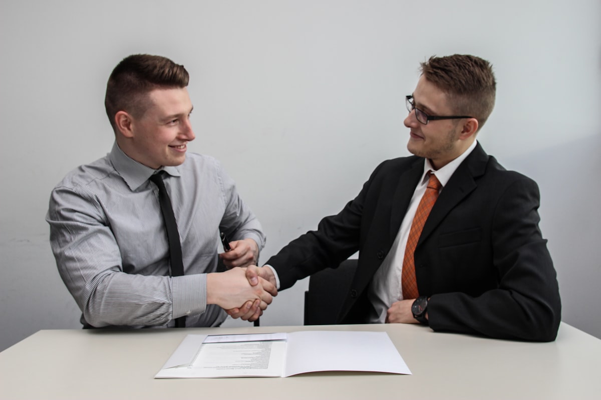 Two business partners shaking hands over a signed agreement